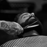 grayscale photography of person holding scissor clipping man's beard