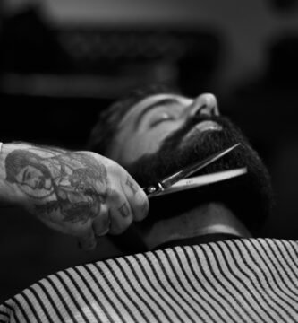grayscale photography of person holding scissor clipping man's beard